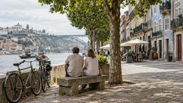 Two people considering a riverside neighbourhood from a shaded bench
