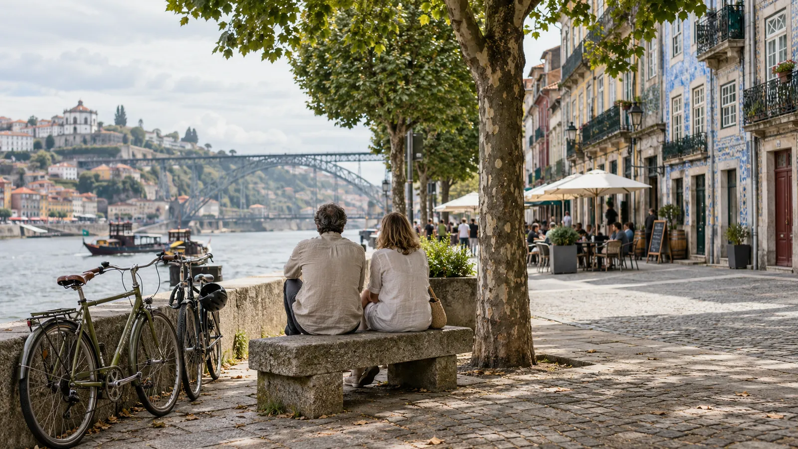 Two people considering a riverside neighbourhood from a shaded bench