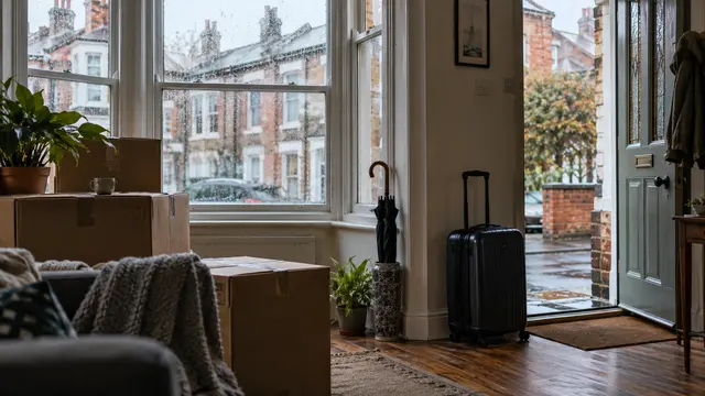 Moving boxes and an umbrella beside a rain-speckled bay window in a British brick terrace home.