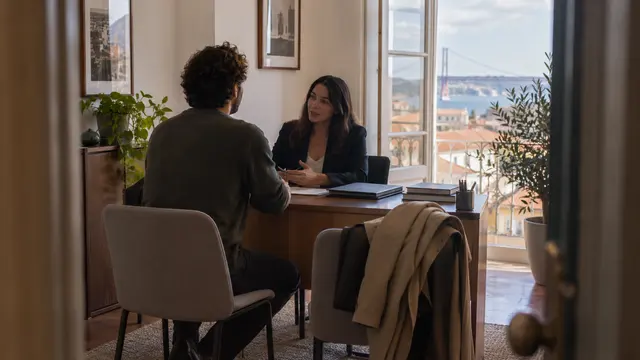A new employee speaking with a human-resources professional across a small office desk.